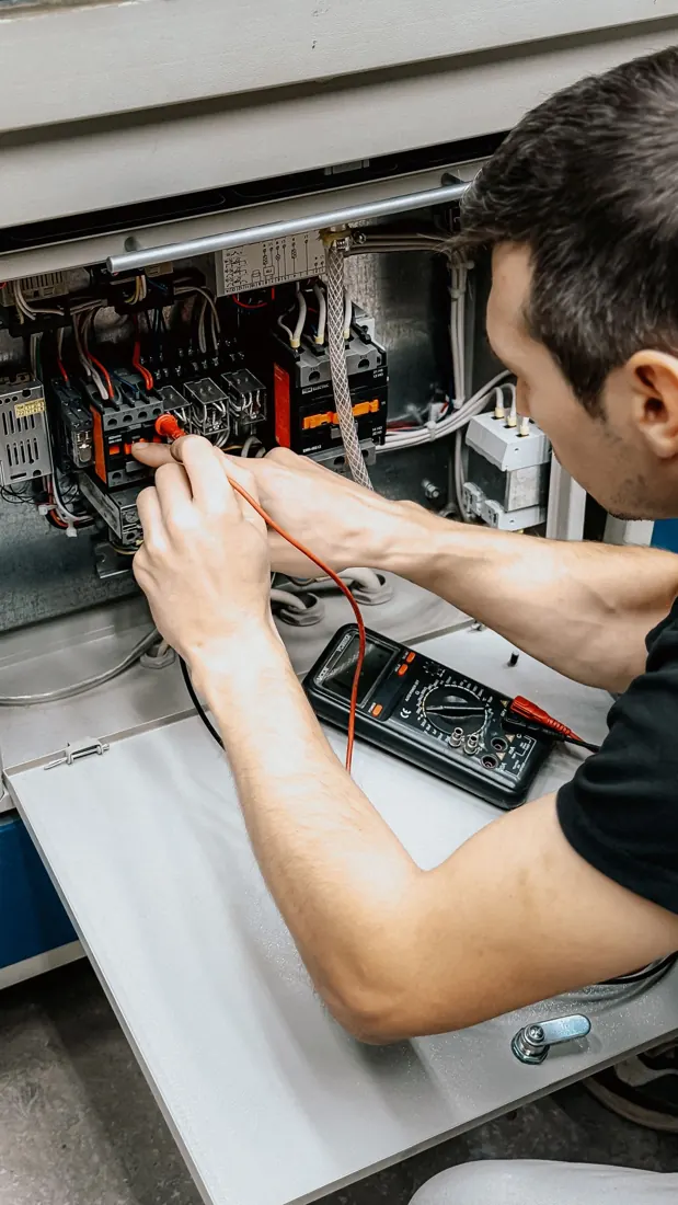 Stock photograph of an electrician testing an electrical panel with a multimeter